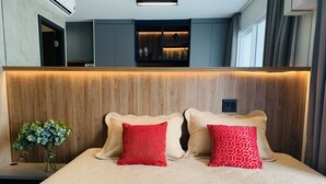 Ein modernes Schlafzimmer mit einem Holzkopfende, zwei roten Kissen mit Muster und einer Vase mit Grünpflanzen auf einem Nachttisch.