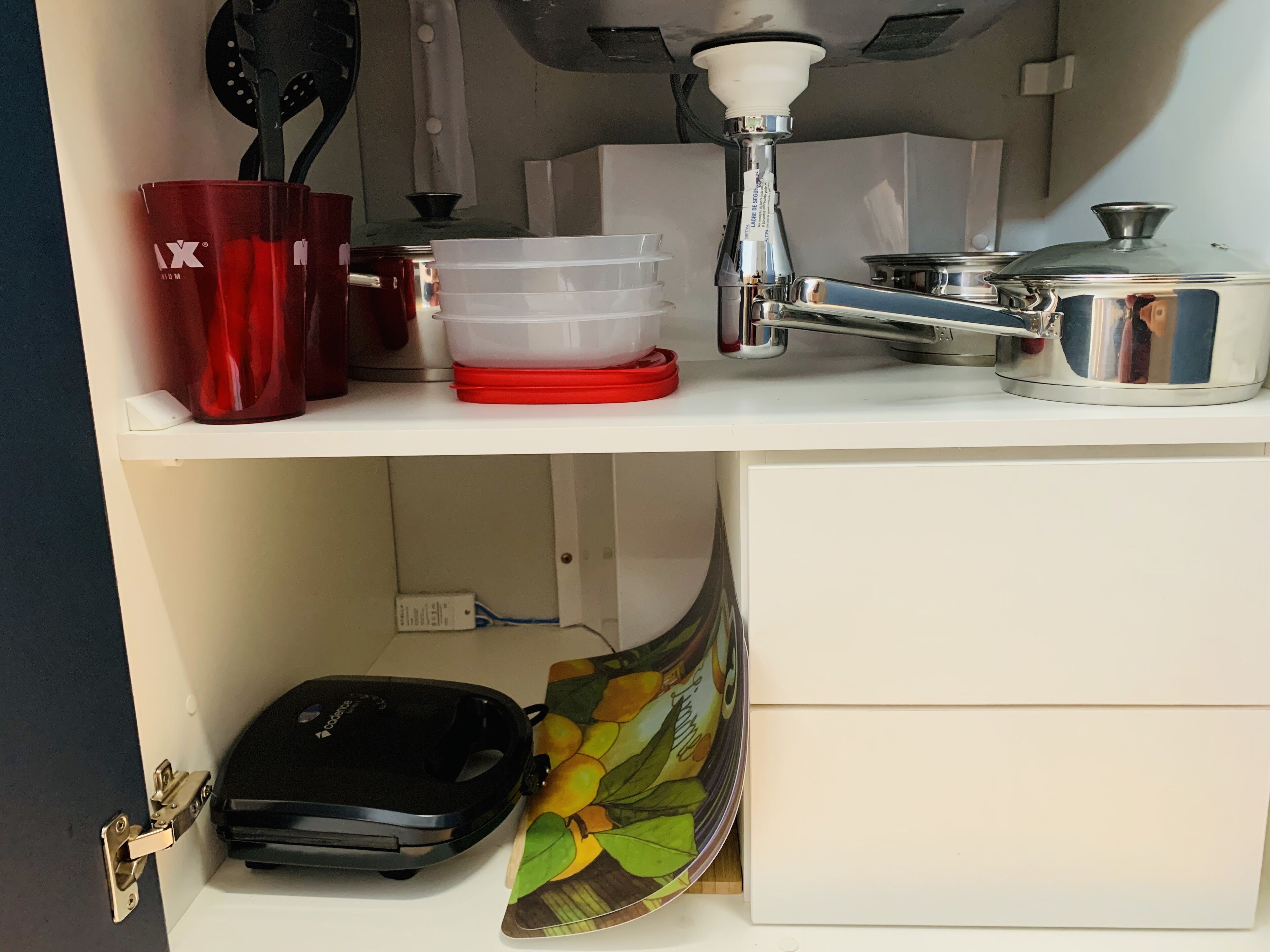 A kitchen counter with a coffee maker, a red mug, a plastic container, and a stainless steel pot.