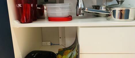 A kitchen counter with a coffee maker, a red mug, a plastic container, and a stainless steel pot.