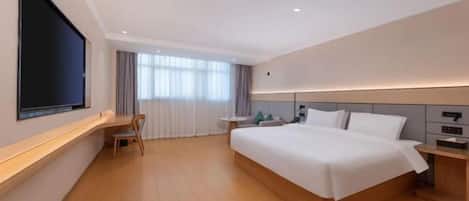 Moderni hotellihuone, jossa on suuri sänky, seinälle asennettu taulutelevisio, työpöytä tuolilla sekä ikkuna, jossa on verhot.