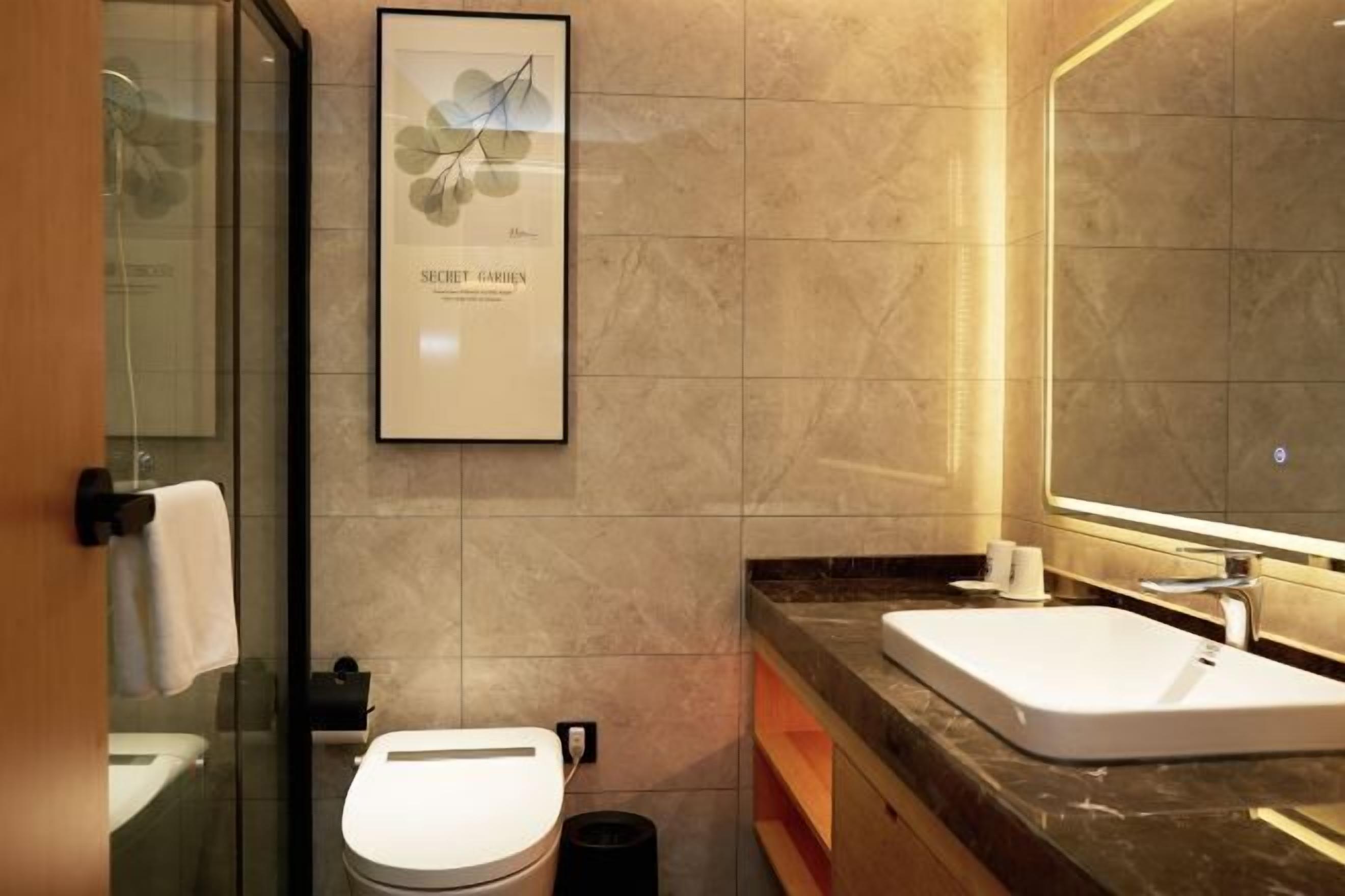 Un bagno moderno con cabina doccia in vetro, un WC bianco, una stampa botanica incorniciata appesa al muro e un grande specchio sopra il lavabo.
