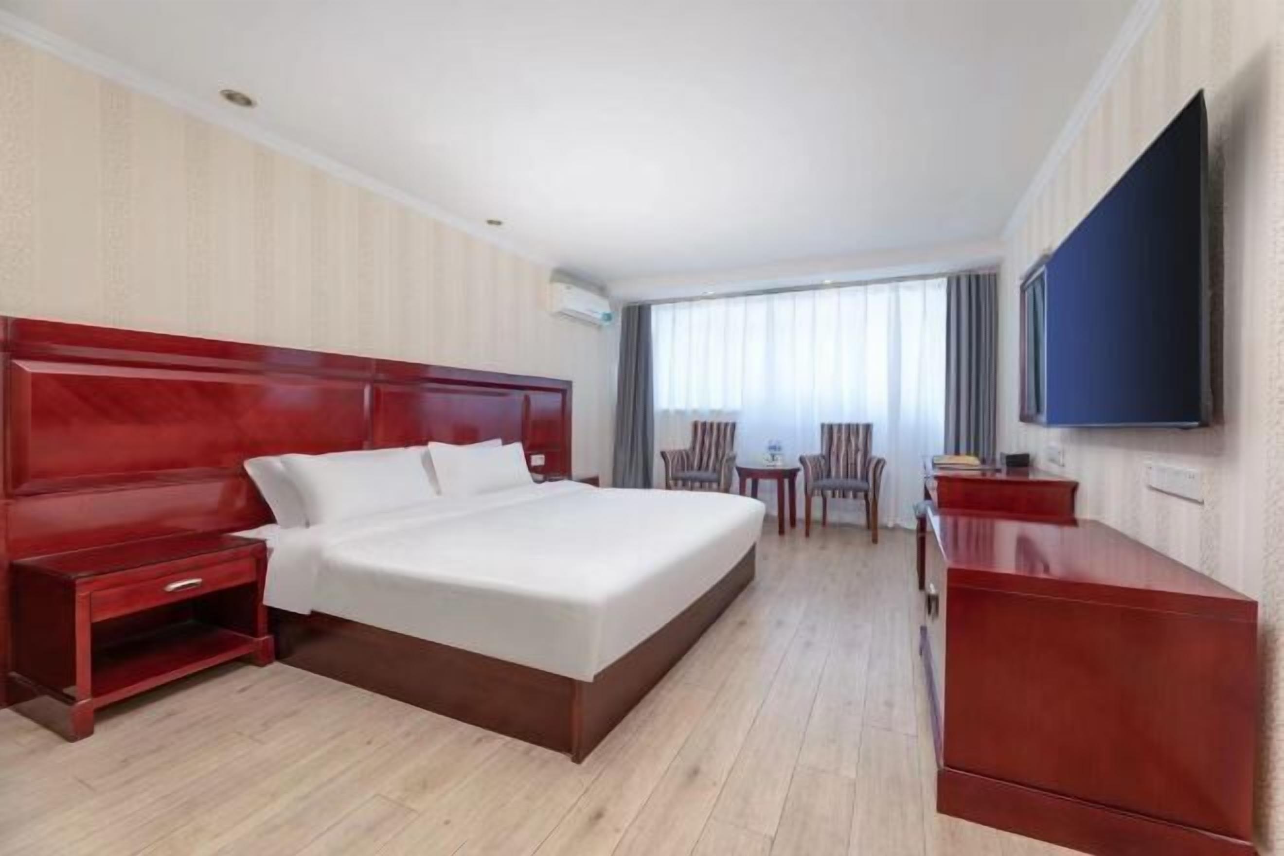A hotel room with a large bed, a desk, a chair, a TV, and a window with curtains.
