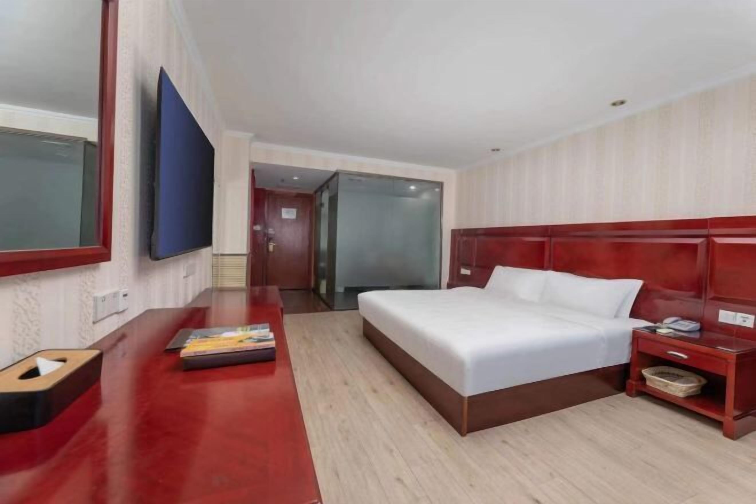 Hotelkamer met een groot bed, een houten bureau, een flatscreen televisie en een glazen deur die leidt naar een andere kamer.