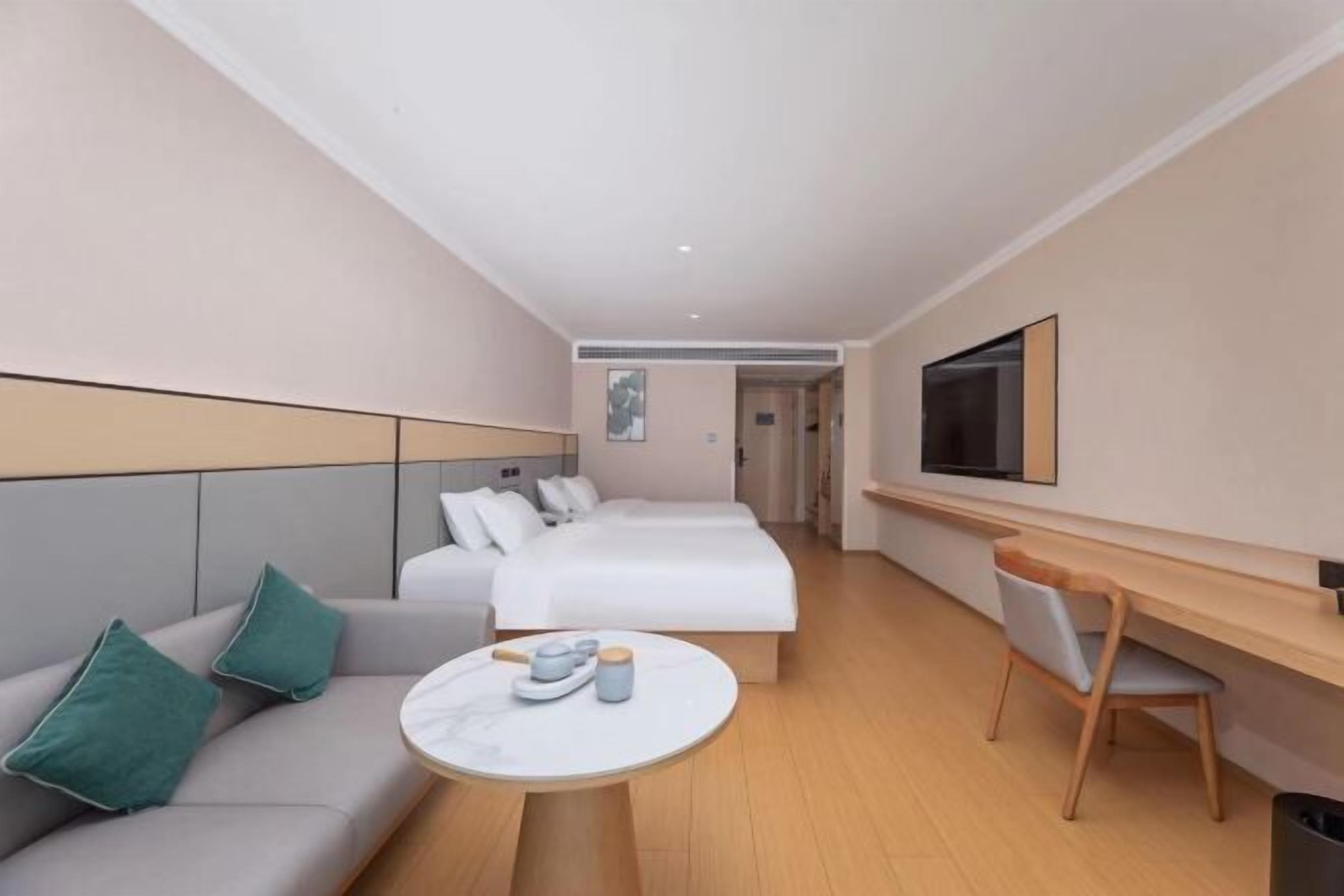 Ein Hotelzimmer mit einer Sitzecke, zwei Betten, einem Schreibtisch und einem Fernseher.