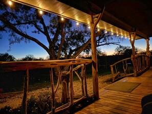 Une terrasse en bois avec une rambarde, des guirlandes lumineuses et des arbres en arrière-plan.
