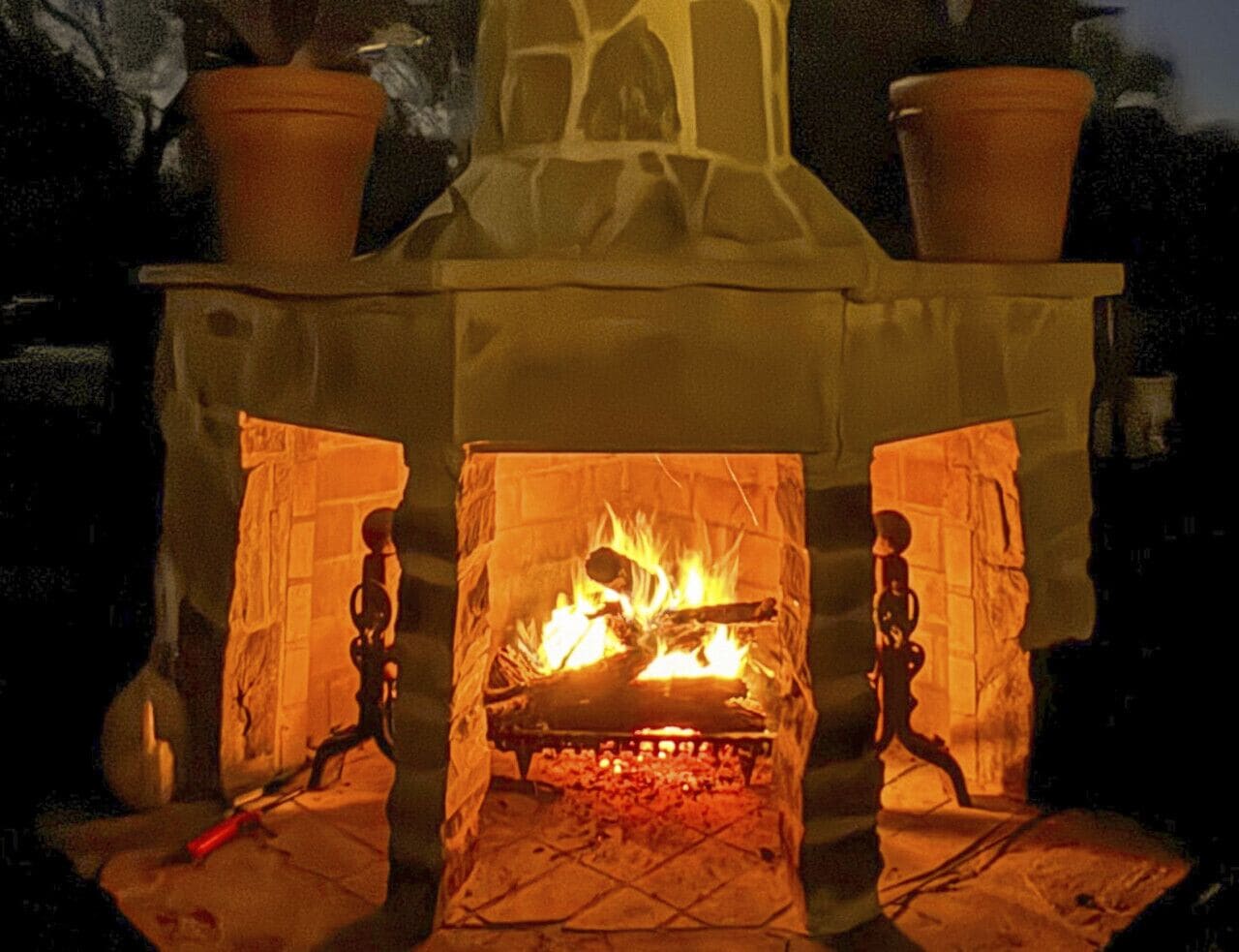 A stone fireplace with a fire burning inside, flanked by two potted plants.