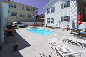 Un espace piscine comprenant des chaises longues, un barbecue et une table de pique-nique.
