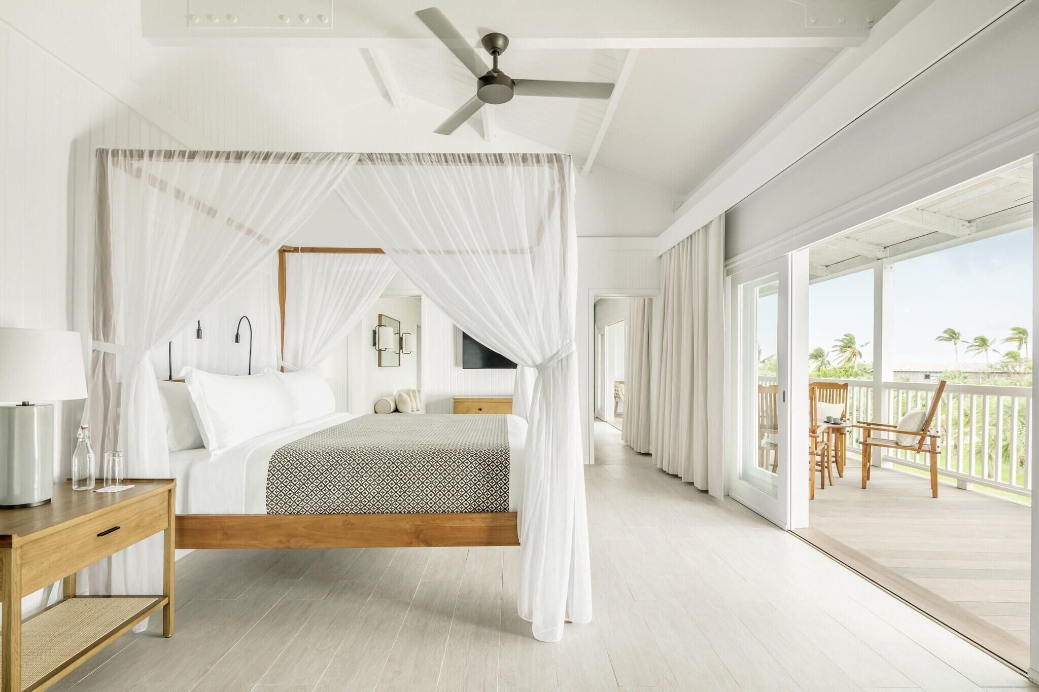 A bedroom with a canopy bed, a ceiling fan, a nightstand, and a view of the balcony.