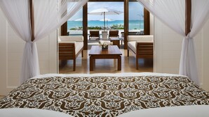 Quarto com uma cama grande, vista para a praia e um espaço de estar com mesa e cadeiras.