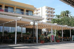 A hotel with outdoor seating, a covered patio, and a multi-story building in the background. - La Nina (Sant Llorenc des Cardassar)