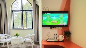 Une pièce avec un téléviseur fixé au mur, deux chaises blanches, une petite table avec une plante et un banc rouge.