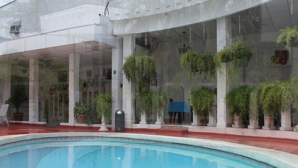 A swimming pool with a clear view of a building with columns and hanging plants. - Grecia Real Hotel (San Salvador)