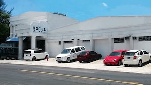 A hotel named "HOTEL GRESIA REAL" with a white facade, parked cars, and a clear blue sky. - Grecia Real Hotel (San Salvador)