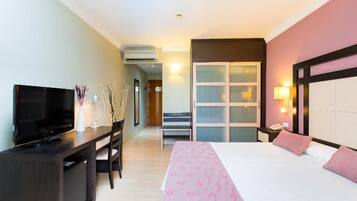 A hotel room with a bed, a desk with a television, a chair, a nightstand, and a wardrobe.