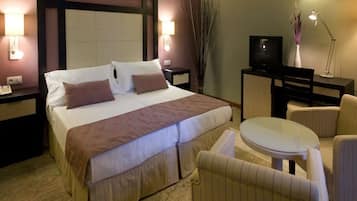 Una habitación de hotel con cama, mesitas de noche, televisión, escritorio y una mesa redonda con sillas.