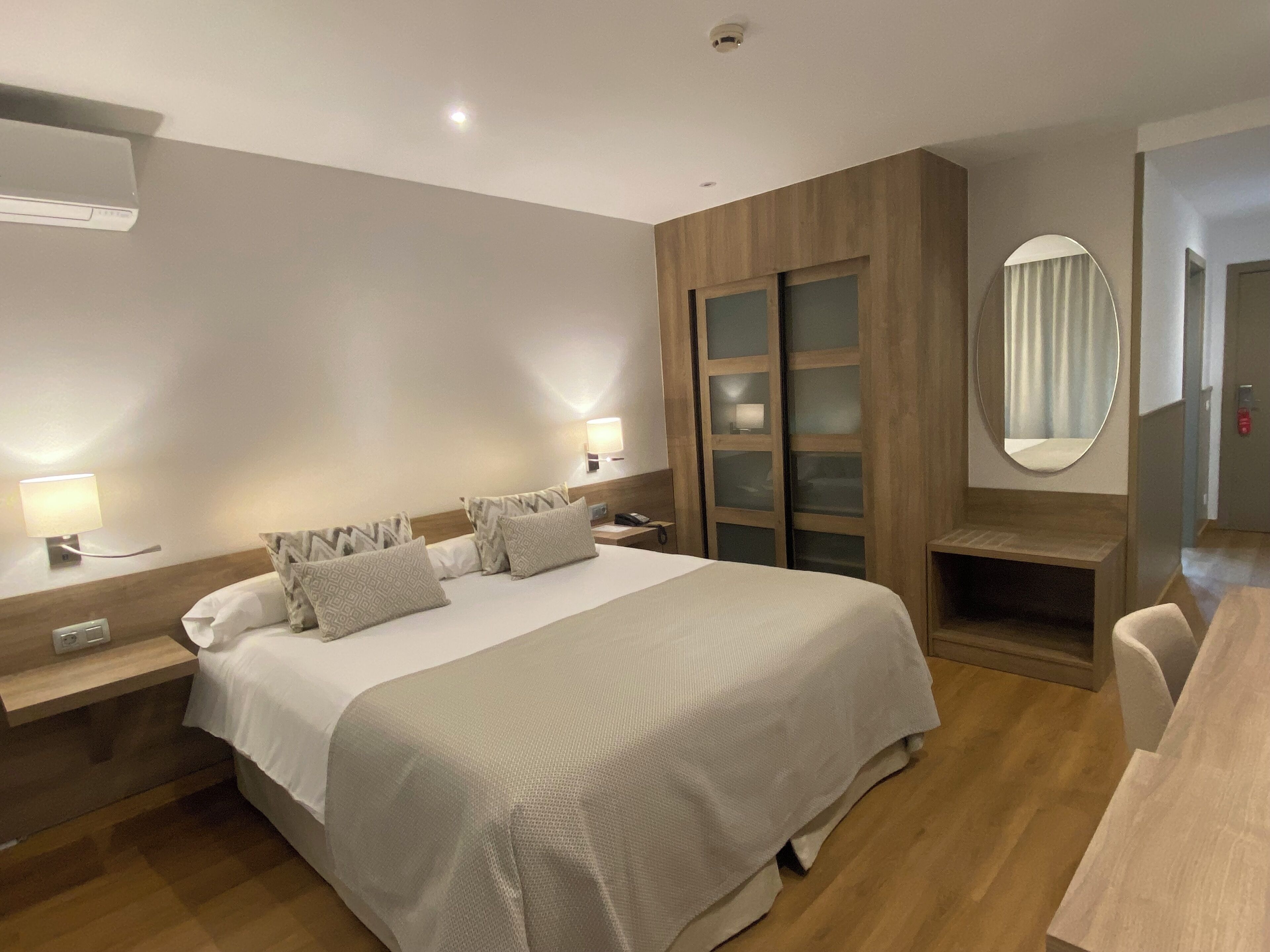Ein Hotelzimmer mit einem großen Bett, Nachttischlampen, einem Holzschrank, einem Spiegel und einem Schreibtisch.