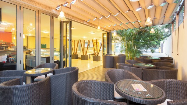 A modern outdoor seating area with wicker furniture and glass tables, overlooking a restaurant and a street view.