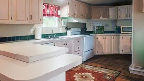 A kitchen with white cabinets, a white countertop, a red patterned rug, and a stove. - Secluded Wildlife Ranch. Kayak on Colorado River. Feed Exotics. (Lometa)