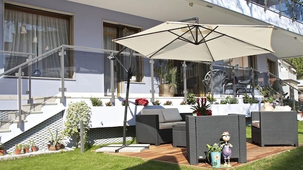 An outdoor patio with wicker furniture, a large umbrella, and potted plants. - My Fair Hotel (Jesolo)