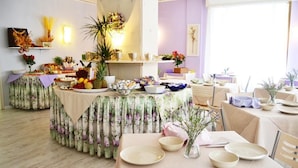 A dining area with multiple tables set for a meal, featuring floral tablecloths and various dishes. - My Fair Hotel (Jesolo)