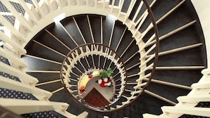 A spiral staircase with a circular design, white railings, and a central area with a rug and flowers. - My Fair Hotel (Jesolo)