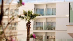A multi-story hotel with balconies, large windows, and a palm tree in the foreground. - Hotel Capricho (Capdepera)