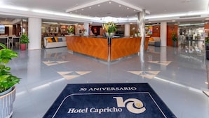 A modern hotel lobby with a reception desk, seating area, and a 50th anniversary carpet. - Hotel Capricho (Capdepera)