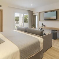 Una habitación de hotel moderna con una cama grande, un sofá, un televisor y un balcón con vistas.