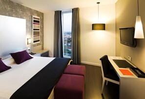 Een hotelkamer met een bed, een bureau, een televisie en uitzicht op de stad.