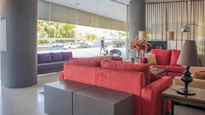 A modern lobby with a red sofa, a grey console, and a large window with a view of the street. - YIT Via Sevilla Mairena (Mairena del Aljarafe)