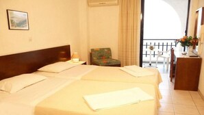 A hotel room with two beds, a chair, a small table, and a balcony with a railing. - Lymiatis Beach Hotel (Karpathos)