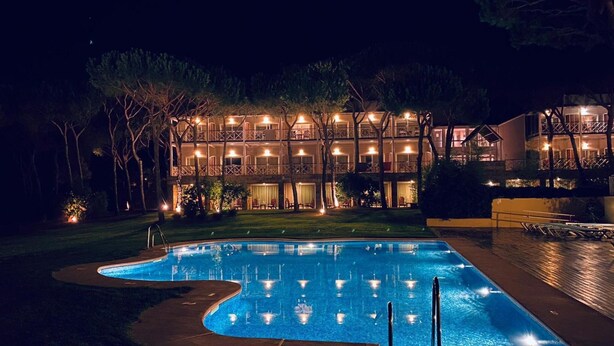 A nighttime view of a hotel with a swimming pool, featuring a multi-story building with balconies and outdoor lighting. - Nuevo Portil Golf (Cartaya)