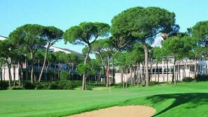 A golf course with a sand bunker, trees, and buildings in the background. - Nuevo Portil Golf (Cartaya)