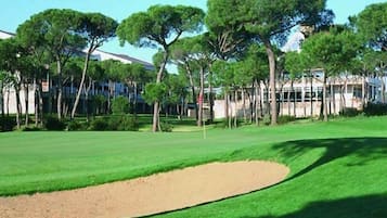 A golf course with a sand bunker, trees, and buildings in the background.