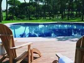 Una terraza de madera con piscina, rodeada de árboles.