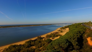 A coastal landscape with a road running alongside a beach, a marina, and dense greenery. - Nuevo Portil Golf (Cartaya)