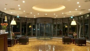 A lobby with a wooden parquet floor, a reception desk with a vase of flowers, and a glass revolving door. - Meditur Hotel Bologna (San Lazzaro di Savena)