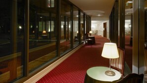 A hotel corridor with a red carpet, a round table with a lamp, and a chair. - Meditur Hotel Bologna (San Lazzaro di Savena)