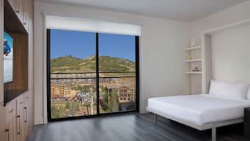 Un dormitorio moderno con un ventanal grande, una cama, un armario de madera y una mesita de noche blanca.