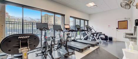 A gym with various exercise equipment, large windows, and a view of buildings.