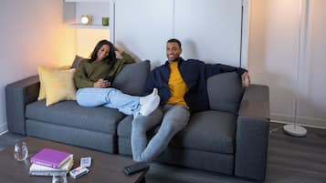 A modern living room with a grey sofa, a coffee table with books and a glass, and a floor lamp.