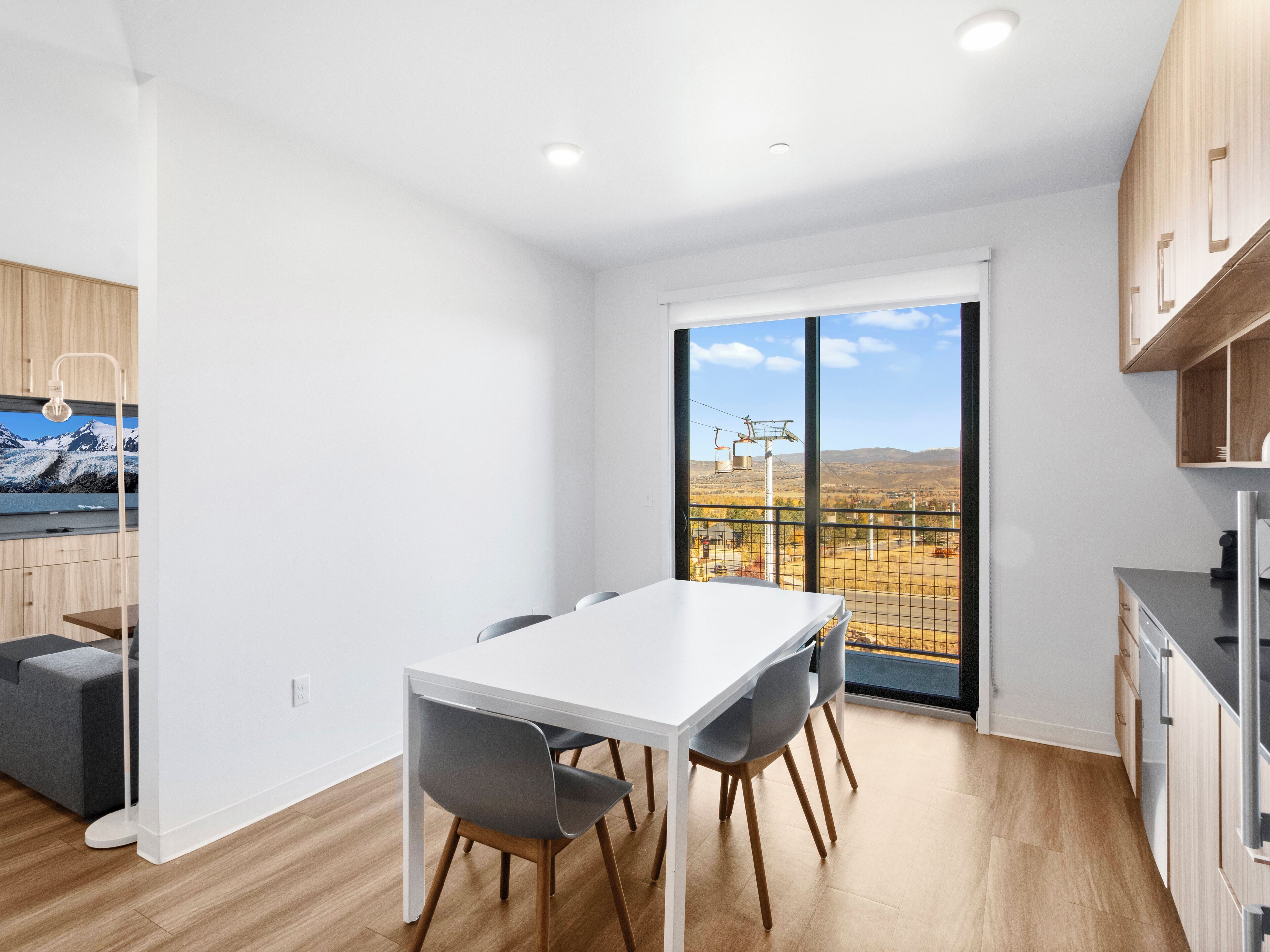 Una cocina moderna con armarios de madera, una encimera blanca y vistas a un paisaje montañoso a través de amplios ventanales.