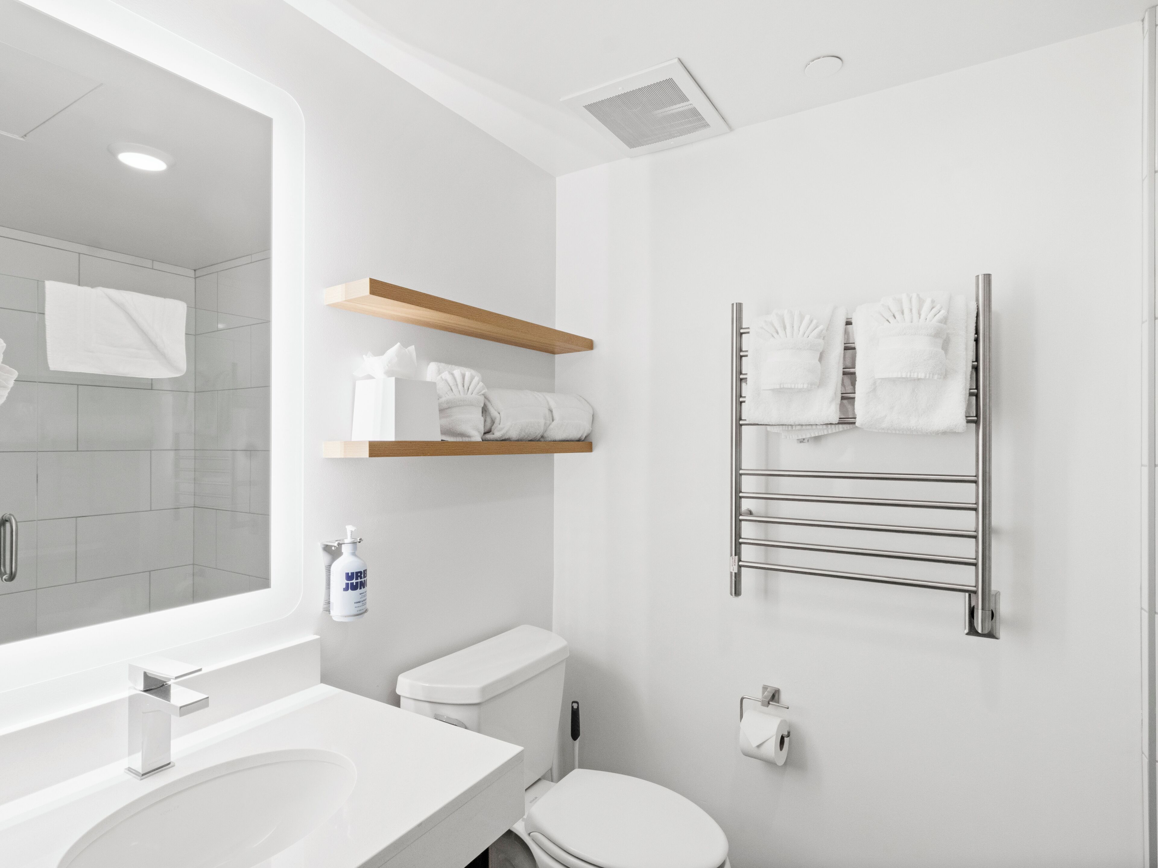 A modern bathroom with a large mirror, a sink, a toilet, and towel racks.