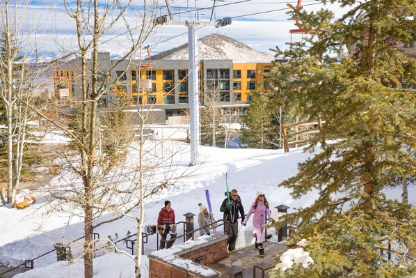 A ski resort with a building in the background, snow-covered ground, and a few people walking.