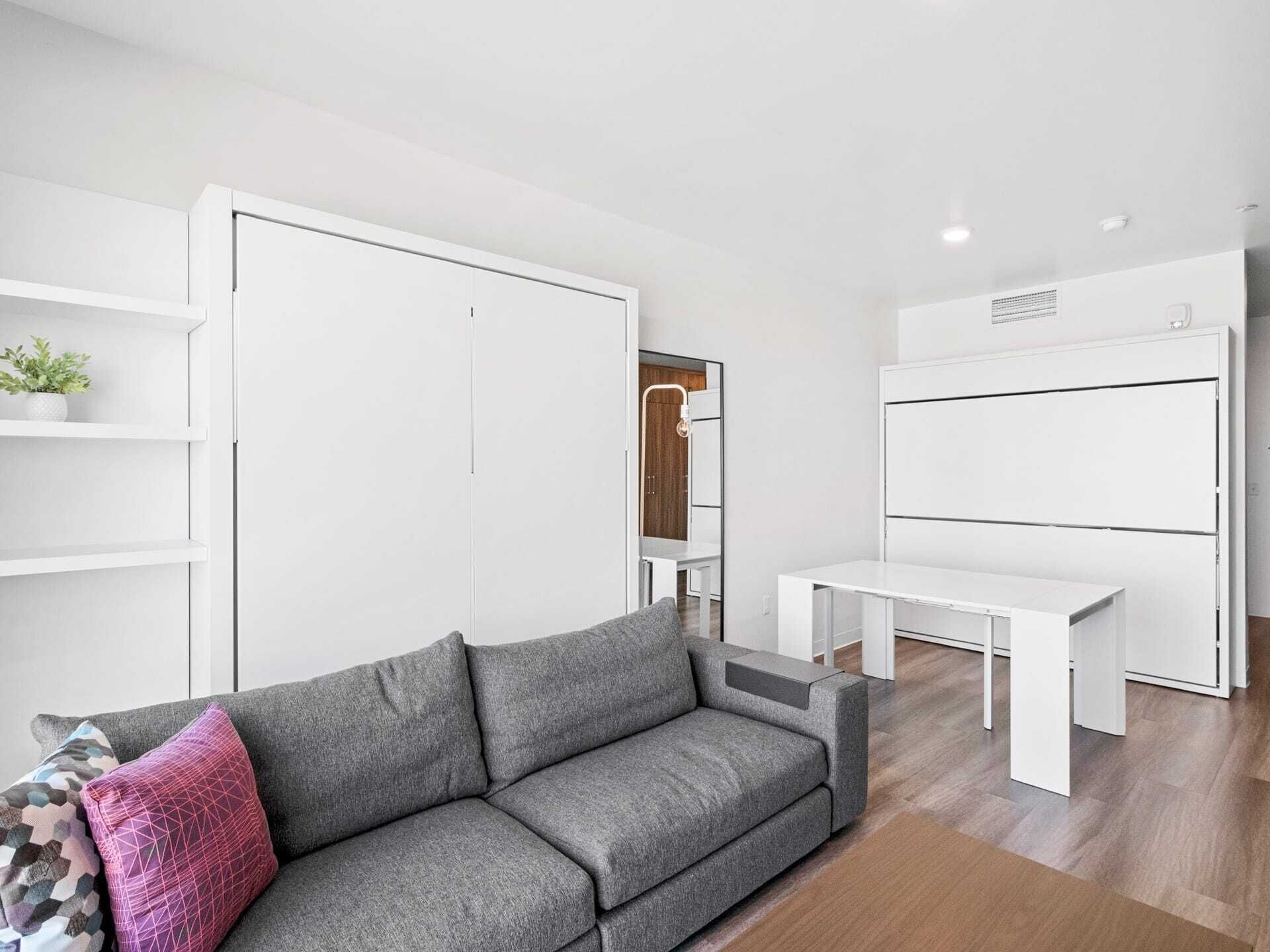 A modern living room with a grey sofa, white shelving units, and a white desk.
