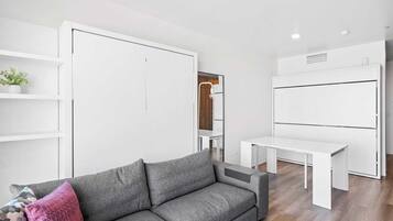 A modern living room with a grey sofa, white shelving units, and a white desk.