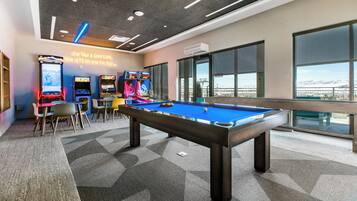 Una mesa de billar en un espacio interior moderno con juegos de arcade y ventanas amplias con vistas.