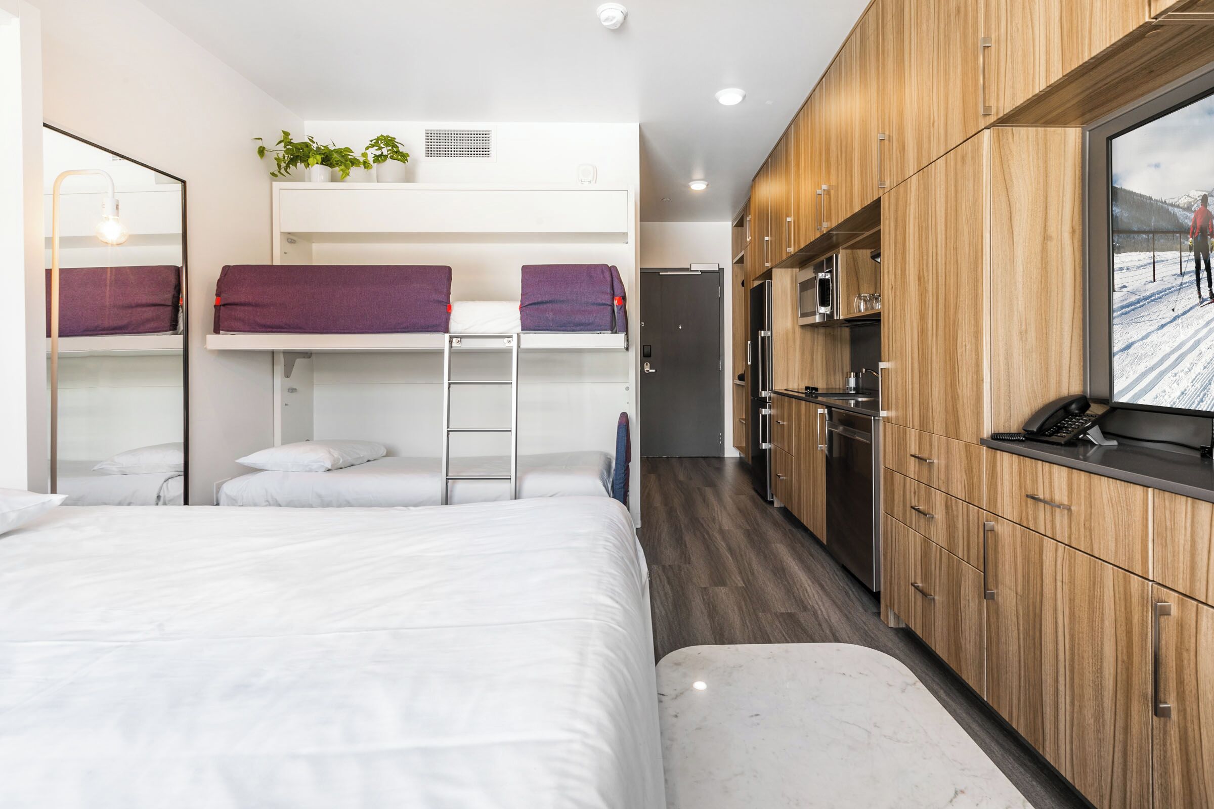 Ein modernes Hotelzimmer mit Etagenbetten, einer Küchenzeile und einem großen Fenster mit Blick auf eine verschneite Landschaft.