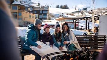 A group of people sitting on a bench near a fire pit in a snowy outdoor setting.