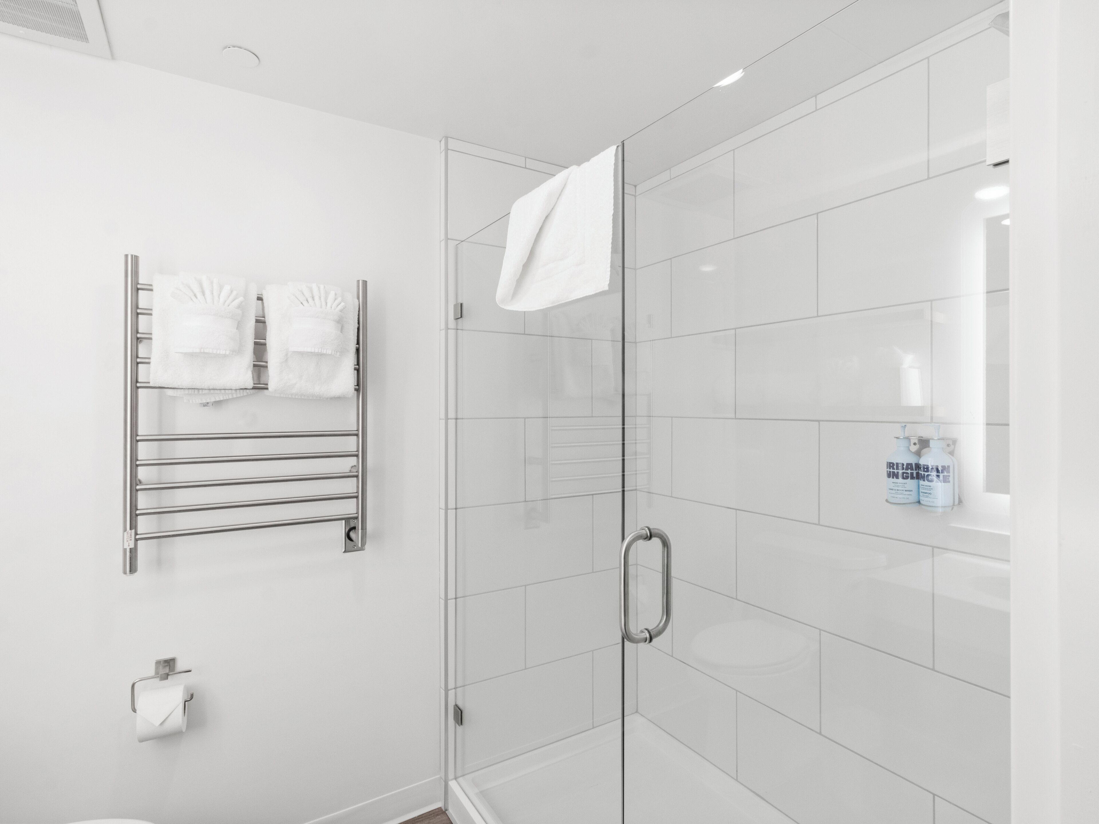 A modern bathroom with a glass shower enclosure, a towel rack with folded towels, and a toilet paper holder.